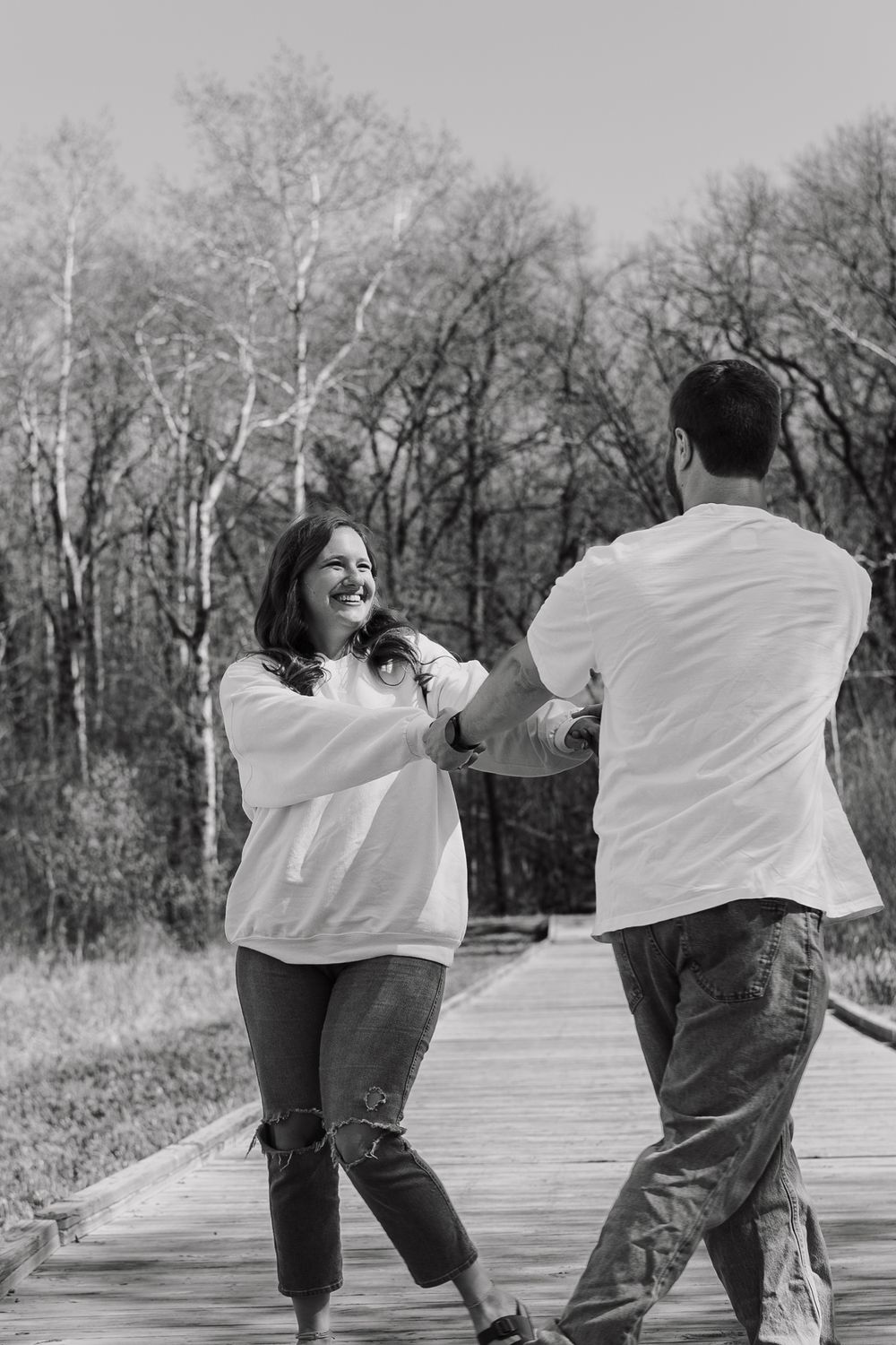 A black and white photo of a couple dancing playfully on a wooden boardwalk.