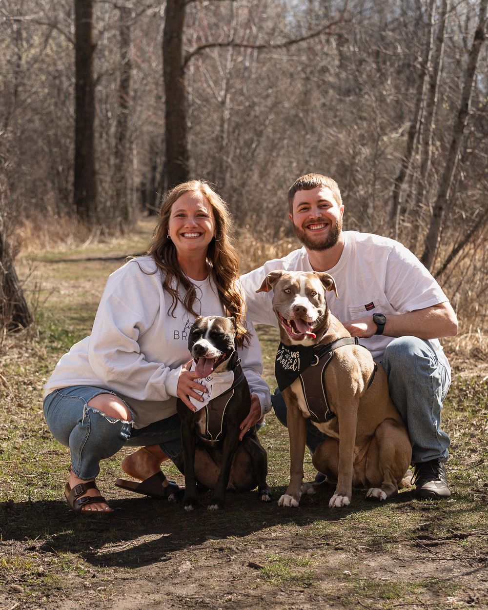 Couple poses with their two rescue dogs in matching white sweaters outdoors.