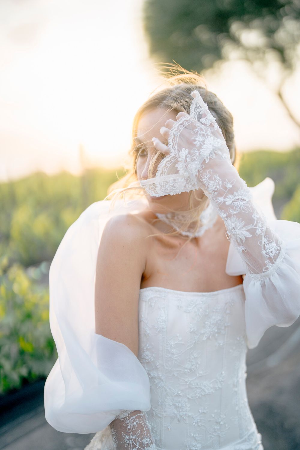 Backlit bridal portrait showcasing detailed lace veil and structured gown sleeves.