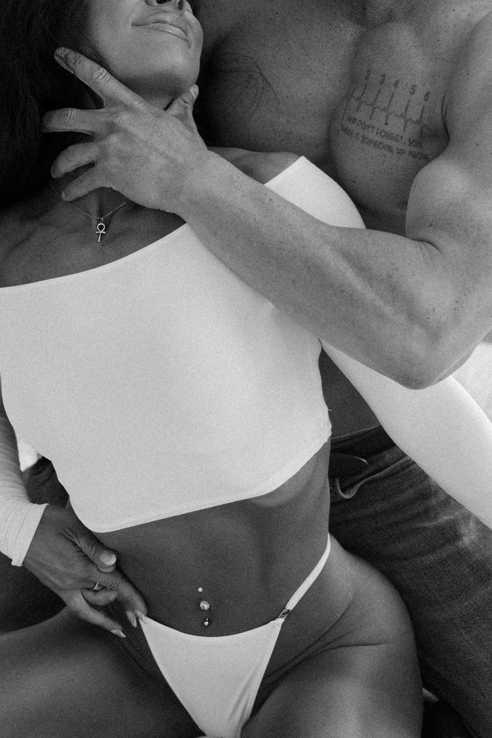 Black and white intimate photo showing a person in white crop top and underwear against another's body.