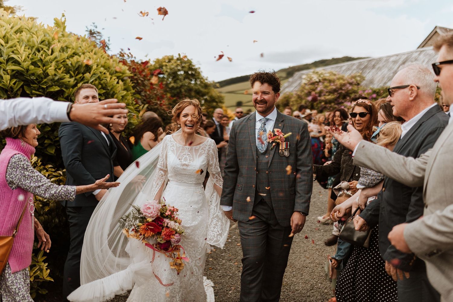 Wedding guests shower happy couple with autumn leaves as they walk along rustic path at Wilde Lodge Wedding Photography