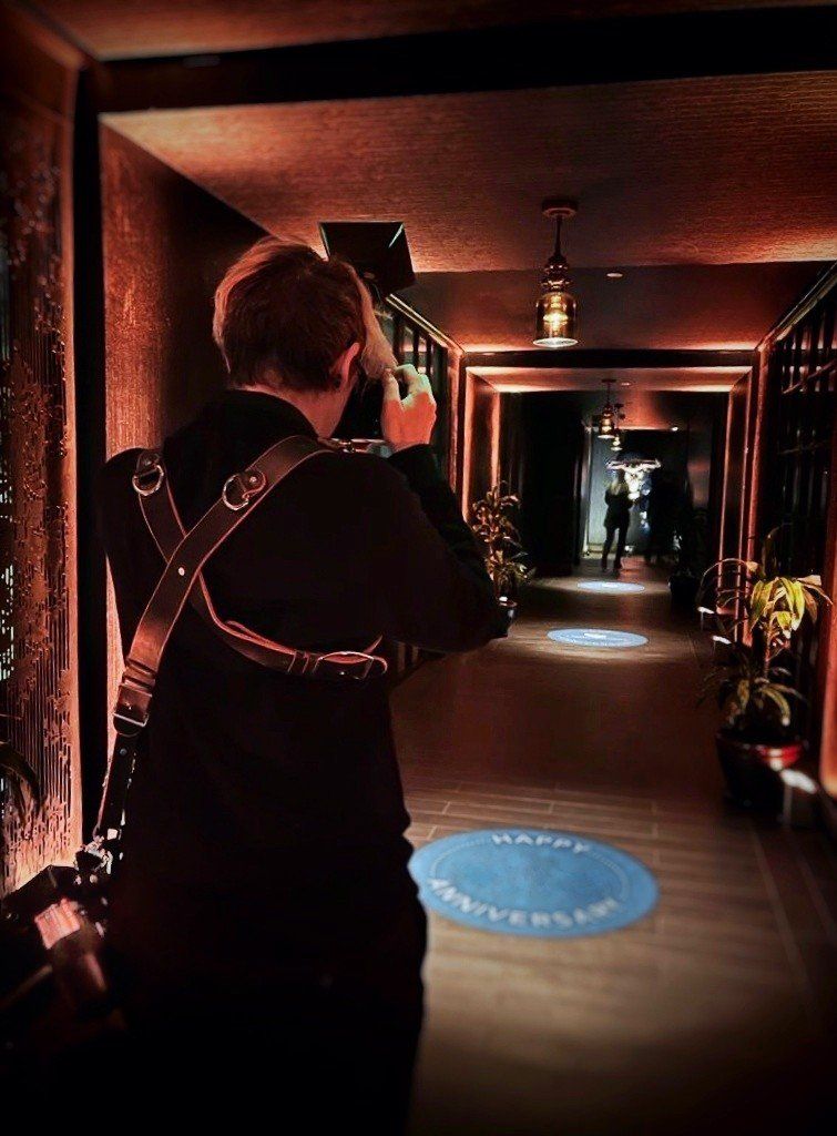Photographer shooting in dimly lit hallway with dramatic red lighting and camera harness.