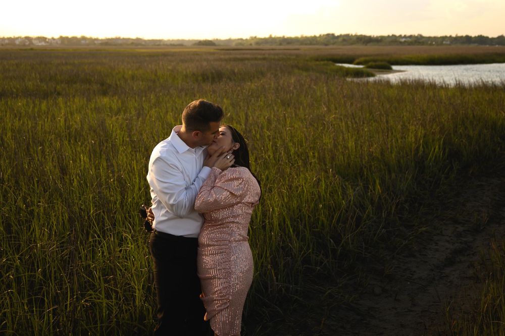 Romantic sunset embrace in tall marsh grass near coastal waters.