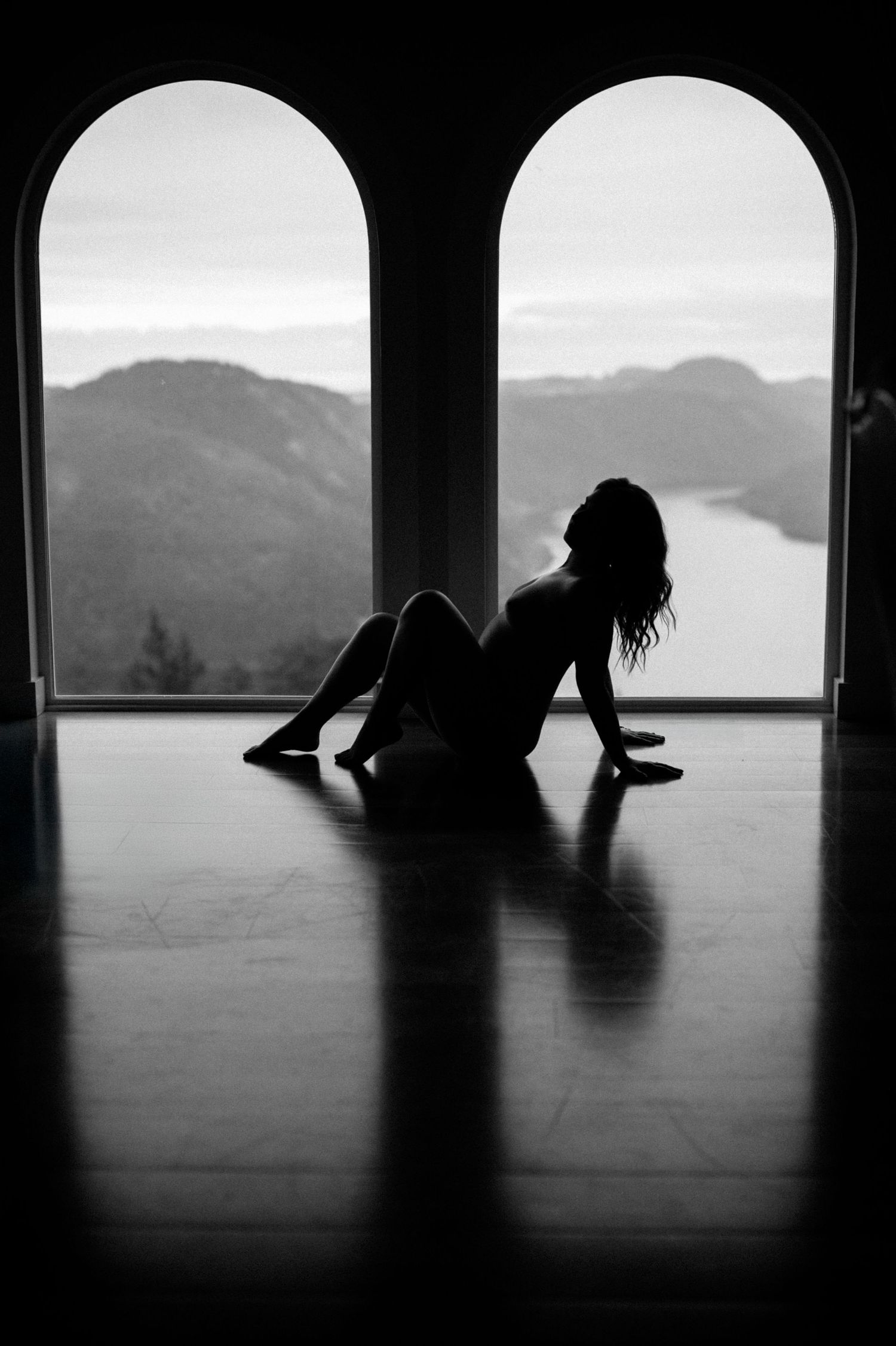 Dramatic silhouette of a figure seated between arched windows with mountain vista beyond.