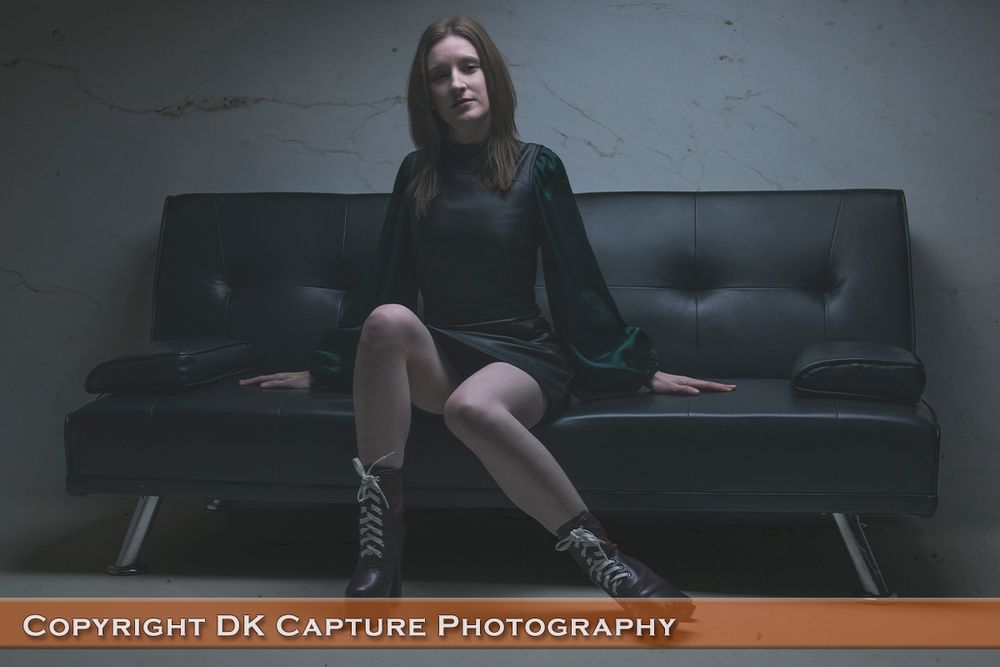 Moody portrait on a black leather couch showing boots and contemporary fashion styling.