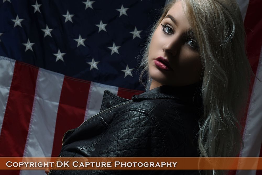 Dramatic portrait with American flag backdrop featuring leather jacket and dramatic side lighting.