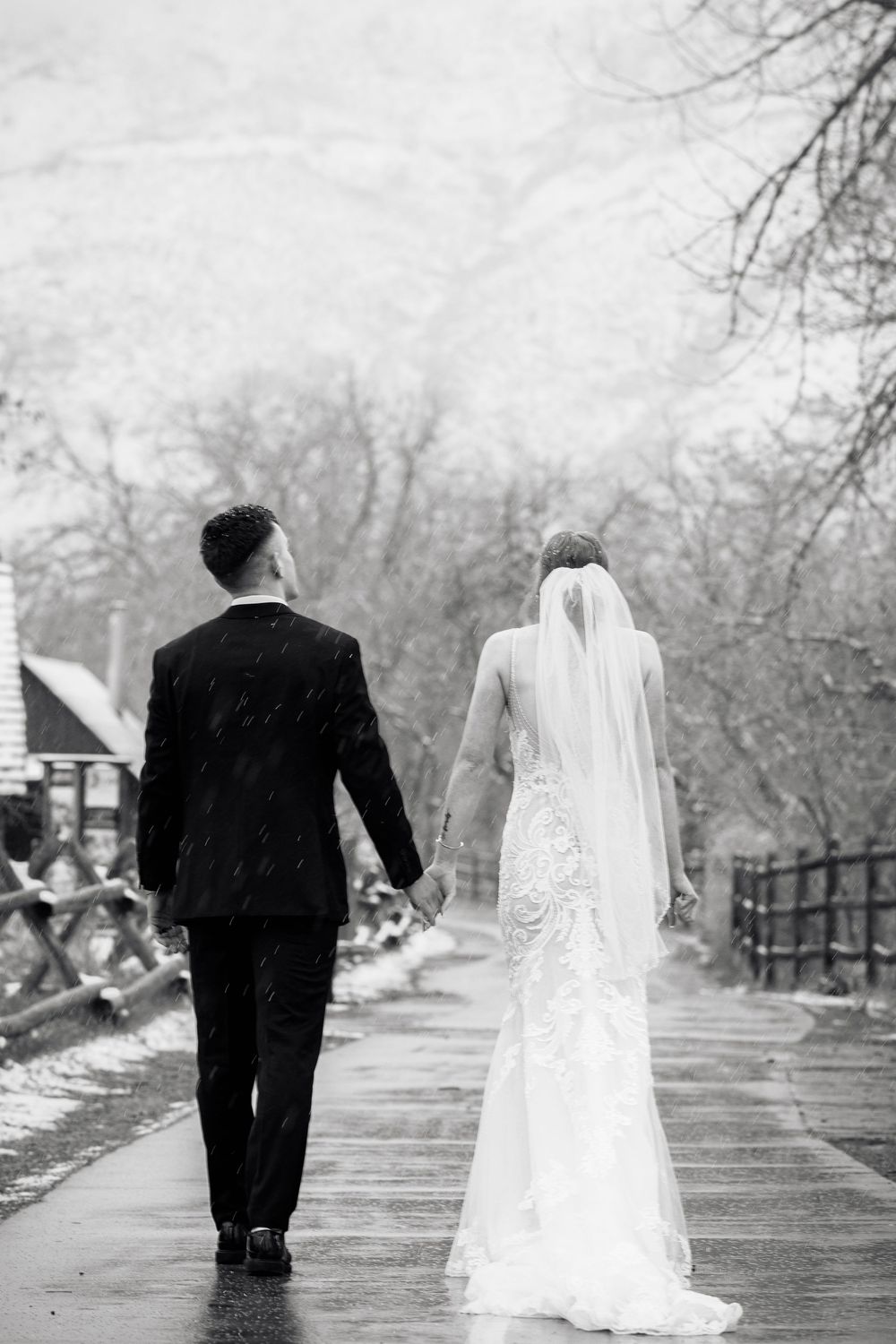 Couple walking hand in hand on a snowy boardwalk in winter wedding attire.