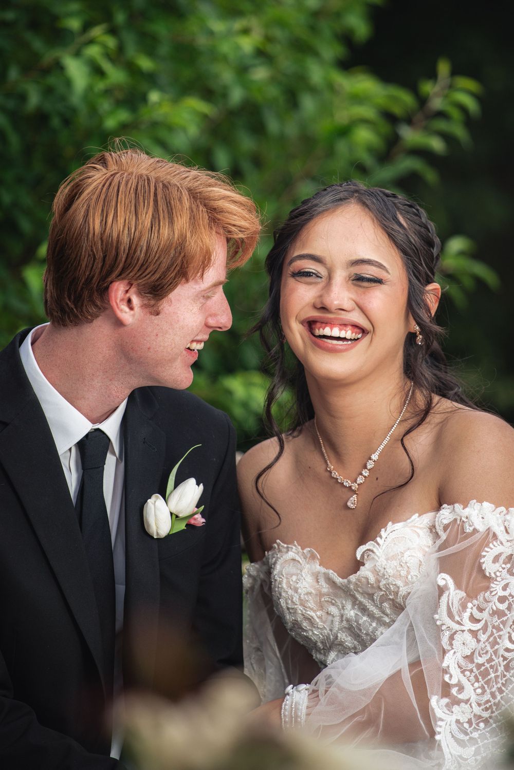 Candid wedding photo capturing joyful laughter in garden setting.