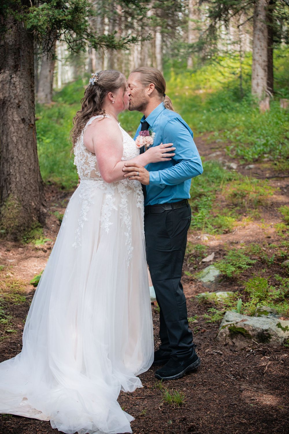 A romantic wedding moment captured in a forest setting with tall pine trees surrounding the couple.
