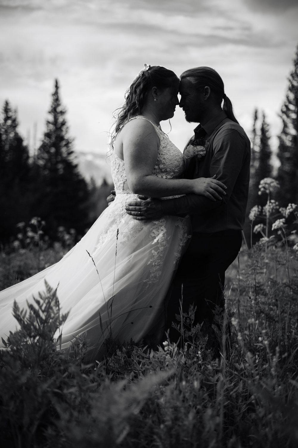 An intimate black and white wedding portrait captured in a mountain wildflower field at dusk.
