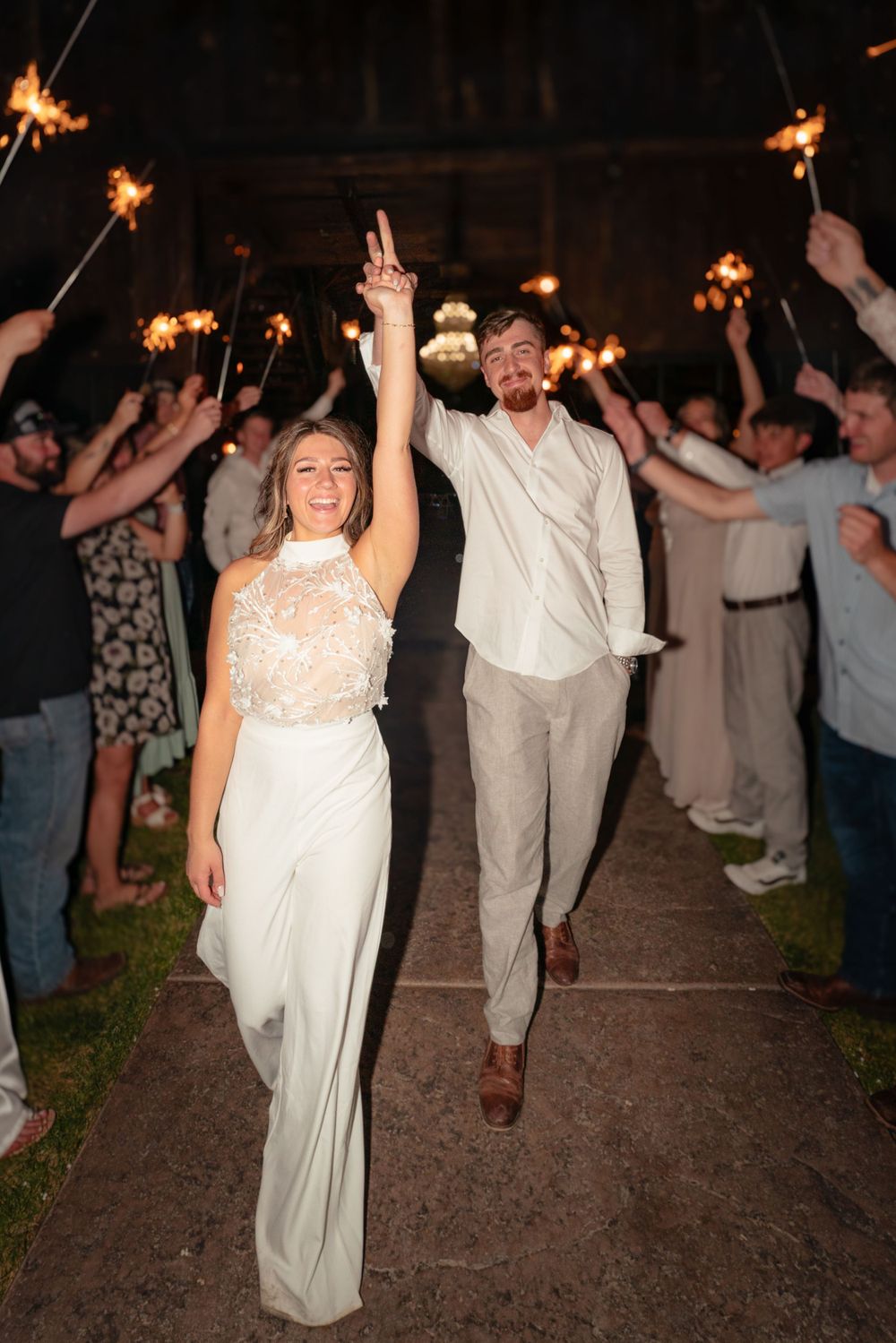 Newlyweds making grand exit through sparkler tunnel held by wedding guests.
