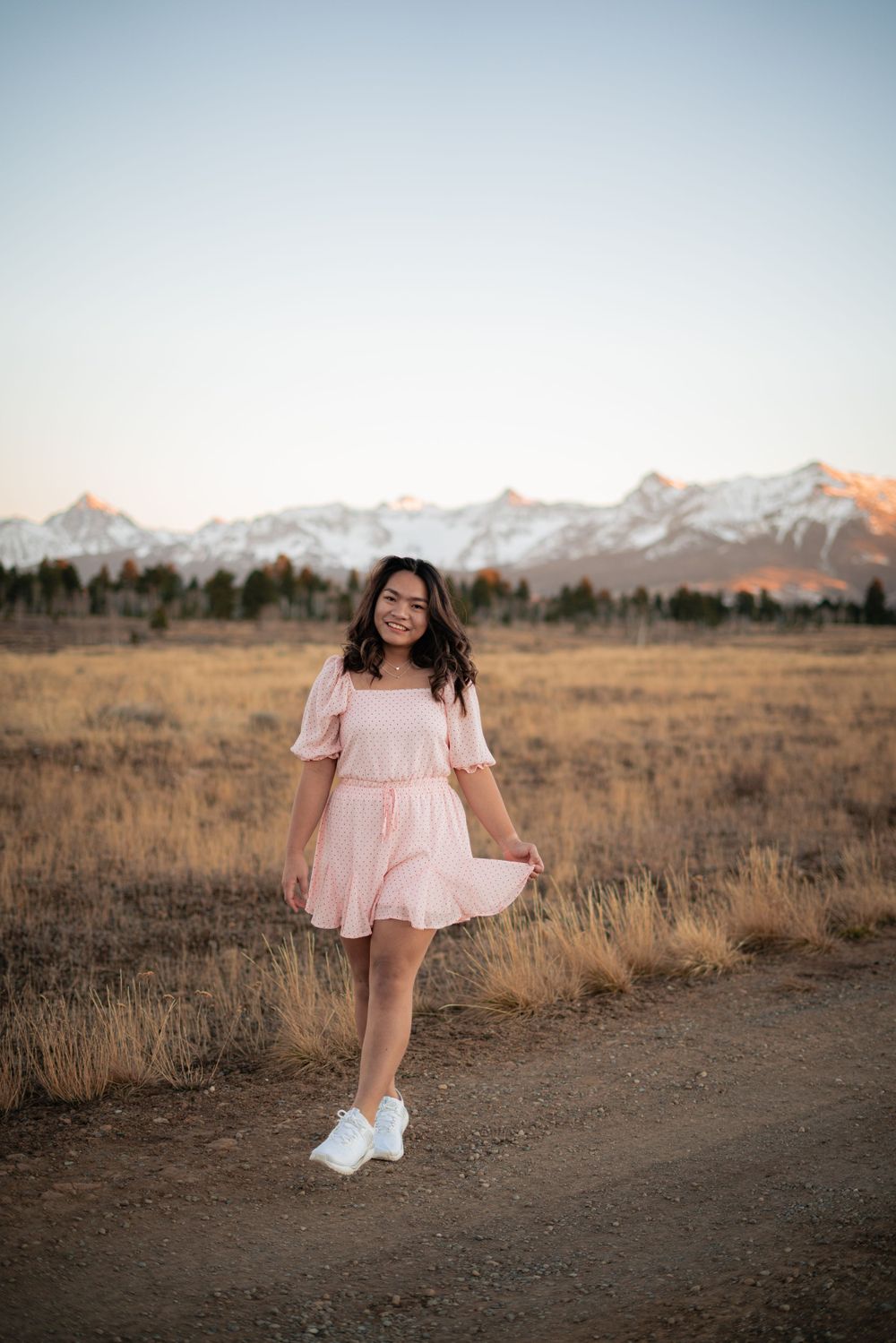 A pink dress twirls against a backdrop of snow-capped mountains and golden grass at sunset.