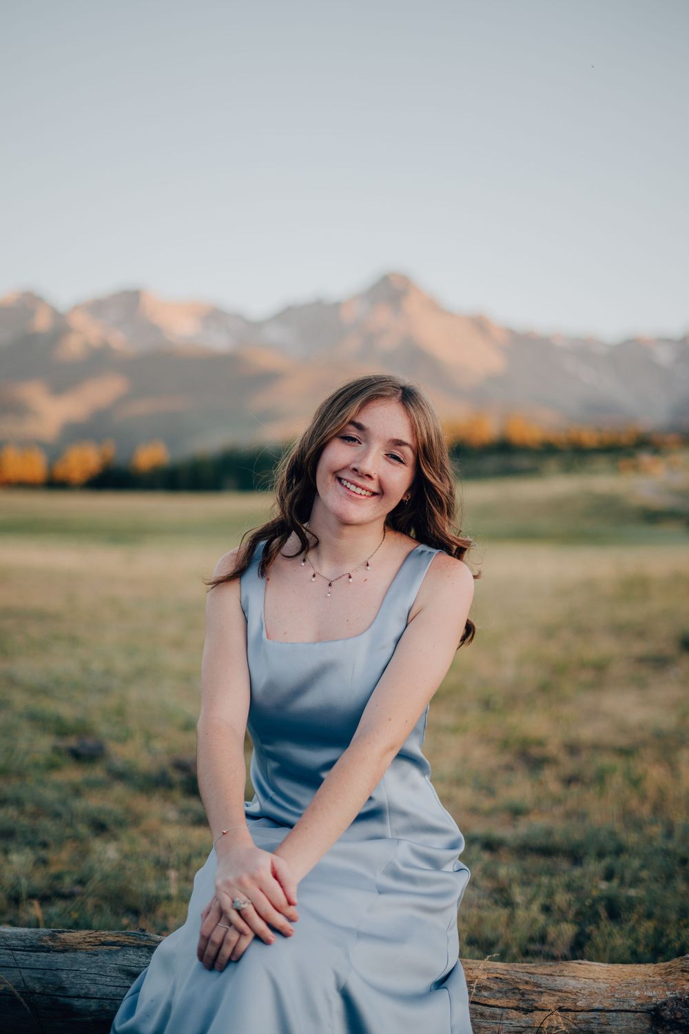 A casual portrait on a log with mountain views featuring a blue sundress.