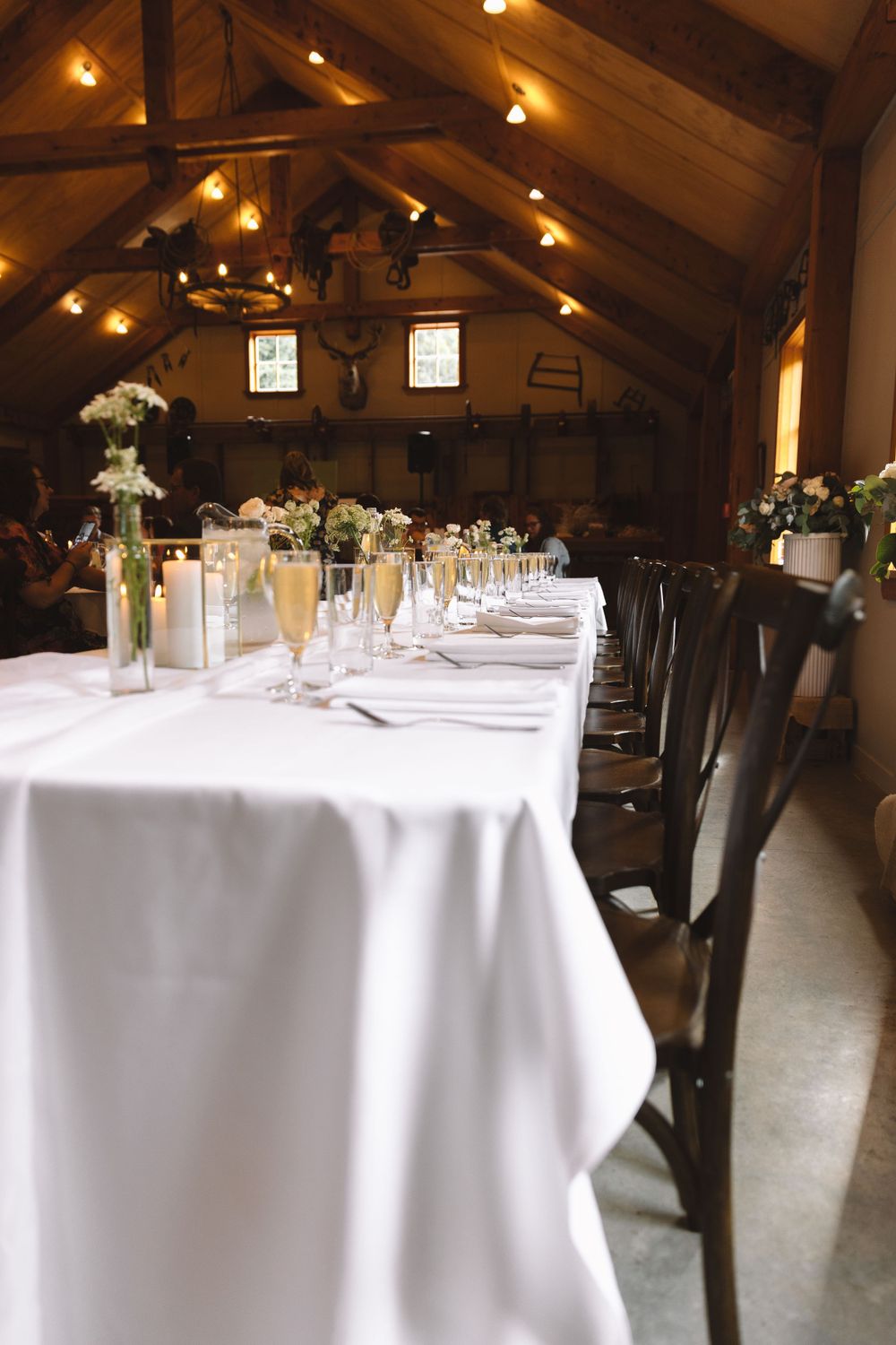 An elegant reception table setting with white linens and string lights in a rustic wooden venue.