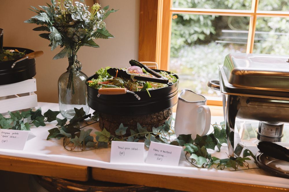 A buffet table with serving dishes and greenery decorations displayed near a sunny window.