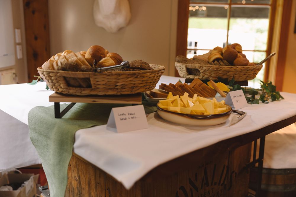 Display of bread baskets and cheese platters on a white tablecloth with green accents.