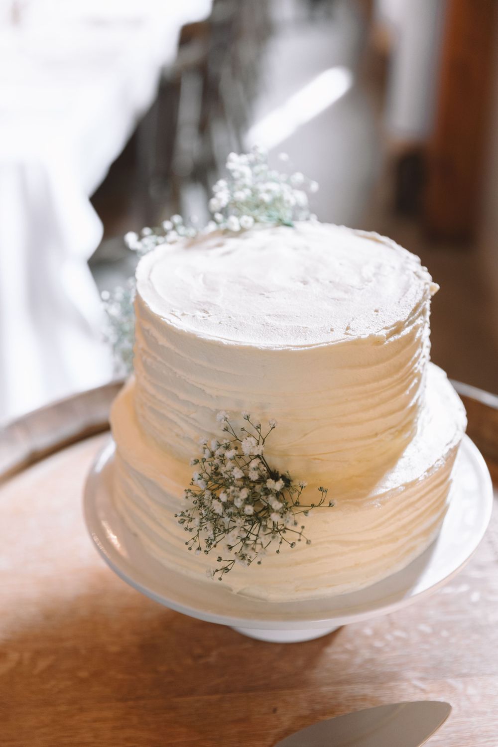 Elegant white wedding cake with textured frosting and sprigs of baby's breath on wooden table.