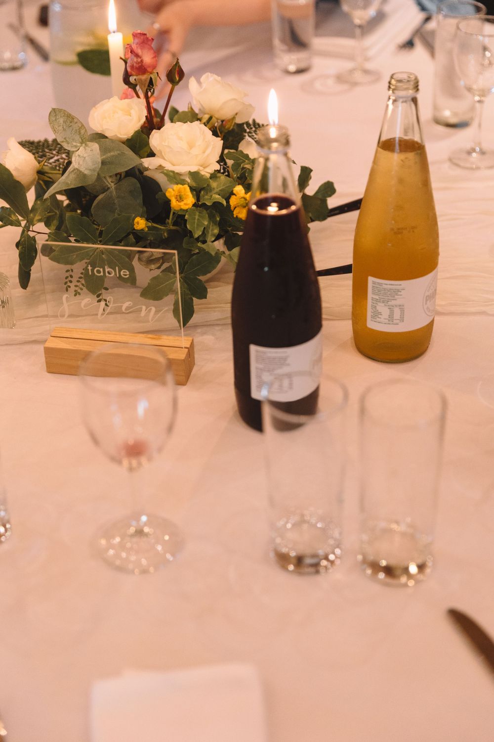 Wedding table setting with floral centerpiece, wine bottles and glasses on white tablecloth.