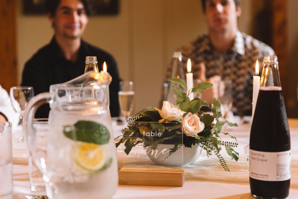 Table setting with floral centerpiece, water pitcher and wine bottles at an indoor event.