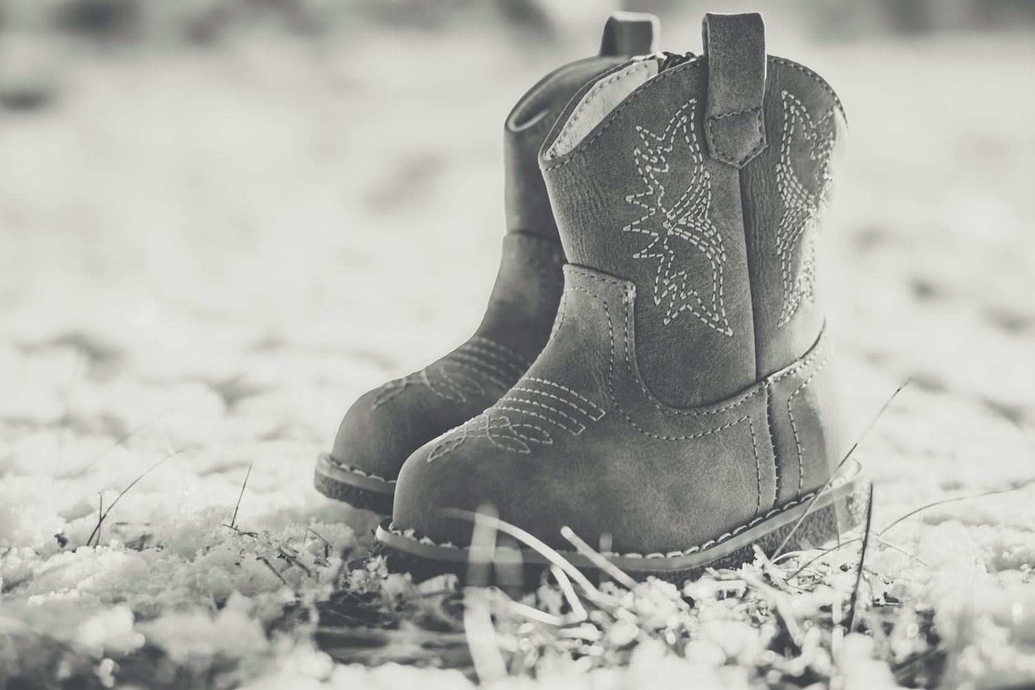 Close-up of gray suede children's cowboy boots with star stitching on textured ground.