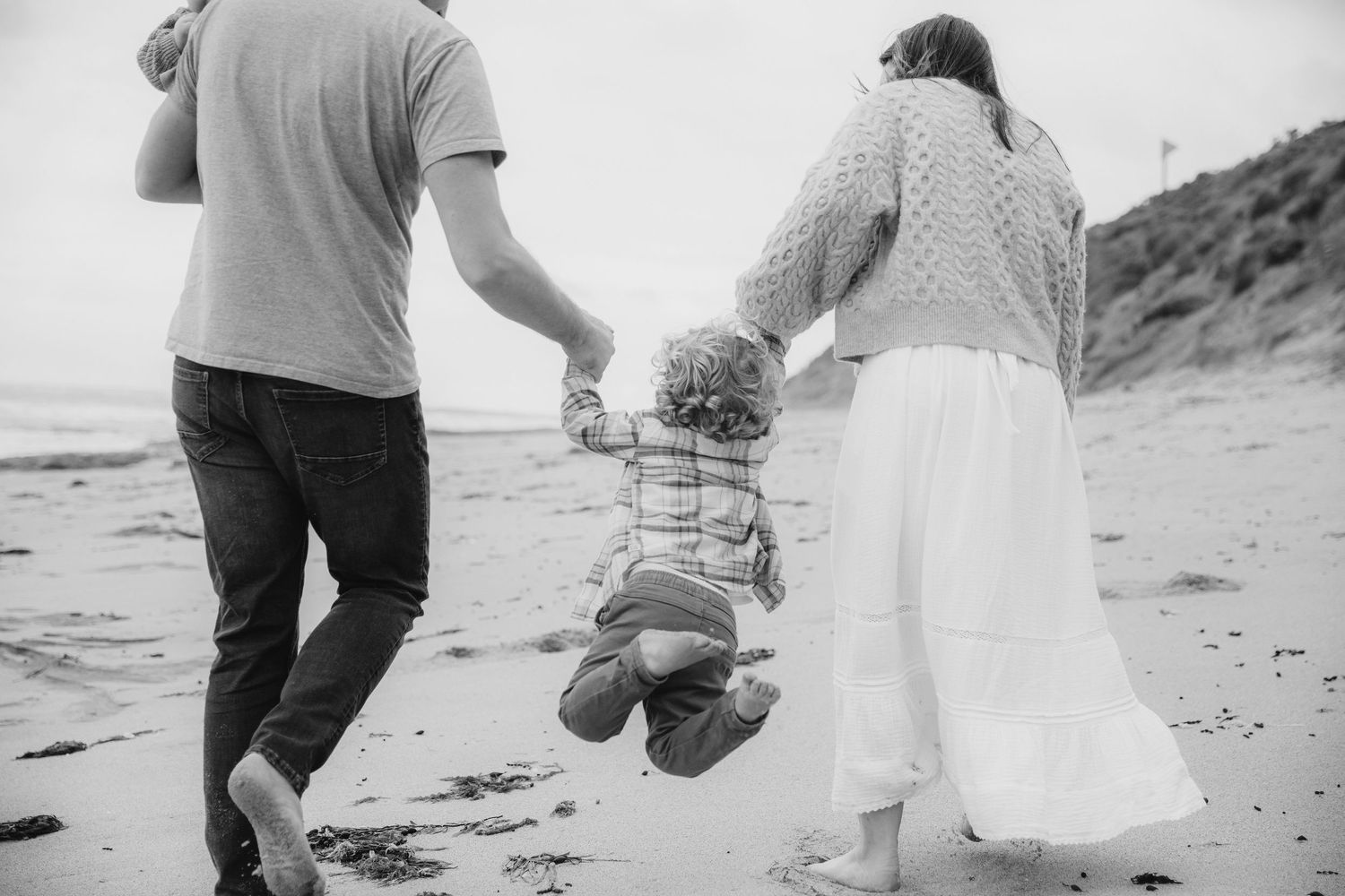 Parents swinging child between them while walking on sandy beach.
