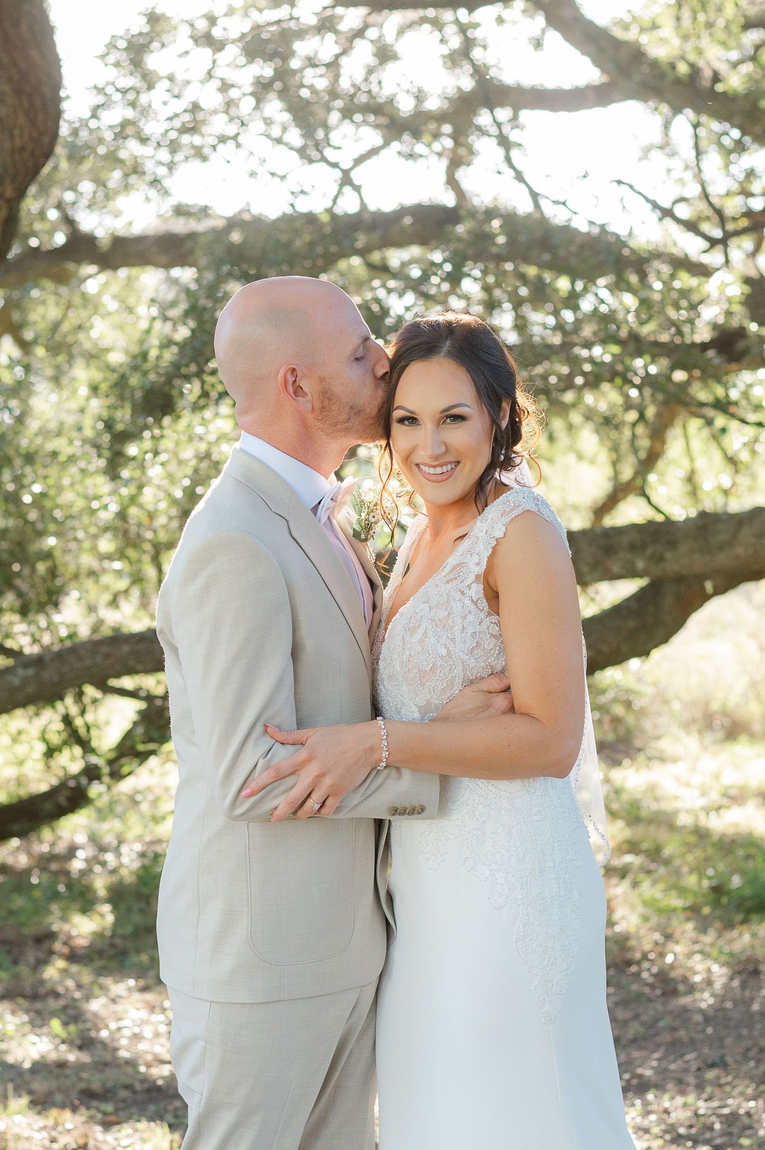 Wedding couple sharing tender moment under oak trees in natural sunlight.