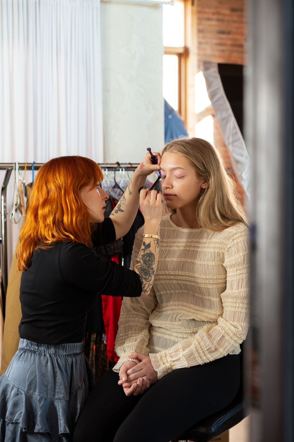 Professional makeup artist applying cosmetics on set in a studio with natural lighting.