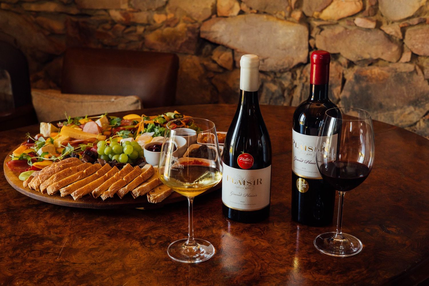 A wooden charcuterie board with meats and cheeses displayed alongside two bottles of wine and filled wine glasses.