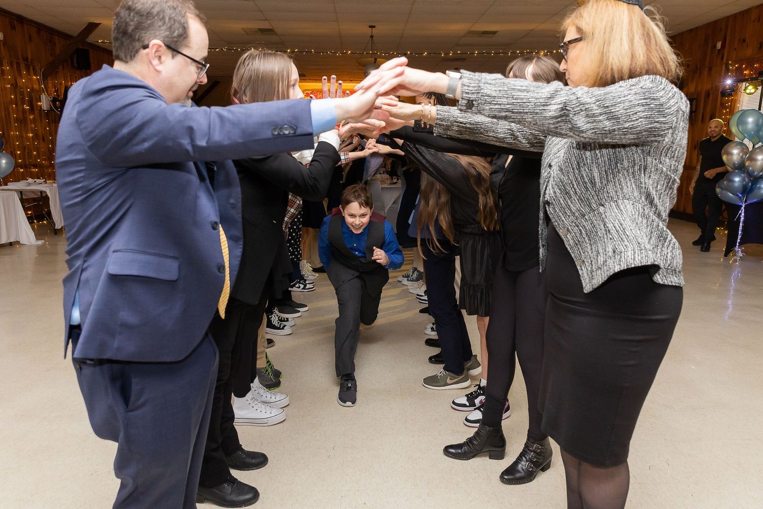 People form a dance tunnel at a celebration event as someone ducks underneath the raised arms.