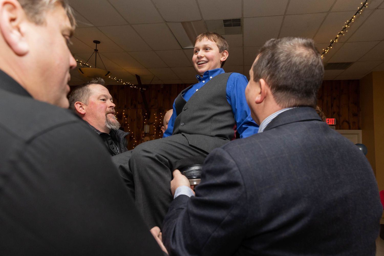 Group lifts young celebrant during festive party in community hall.