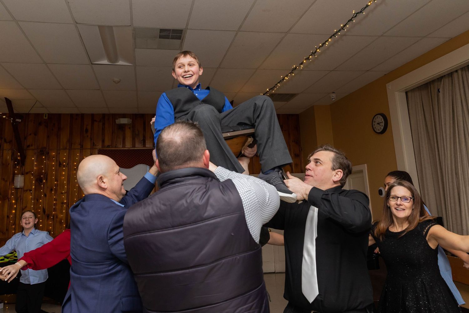 Joyous celebration with group lifting young person in formal attire during event.