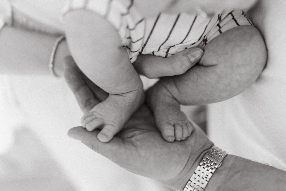 Black and white close-up of tiny baby feet resting on an adult's hand with wristwatch.