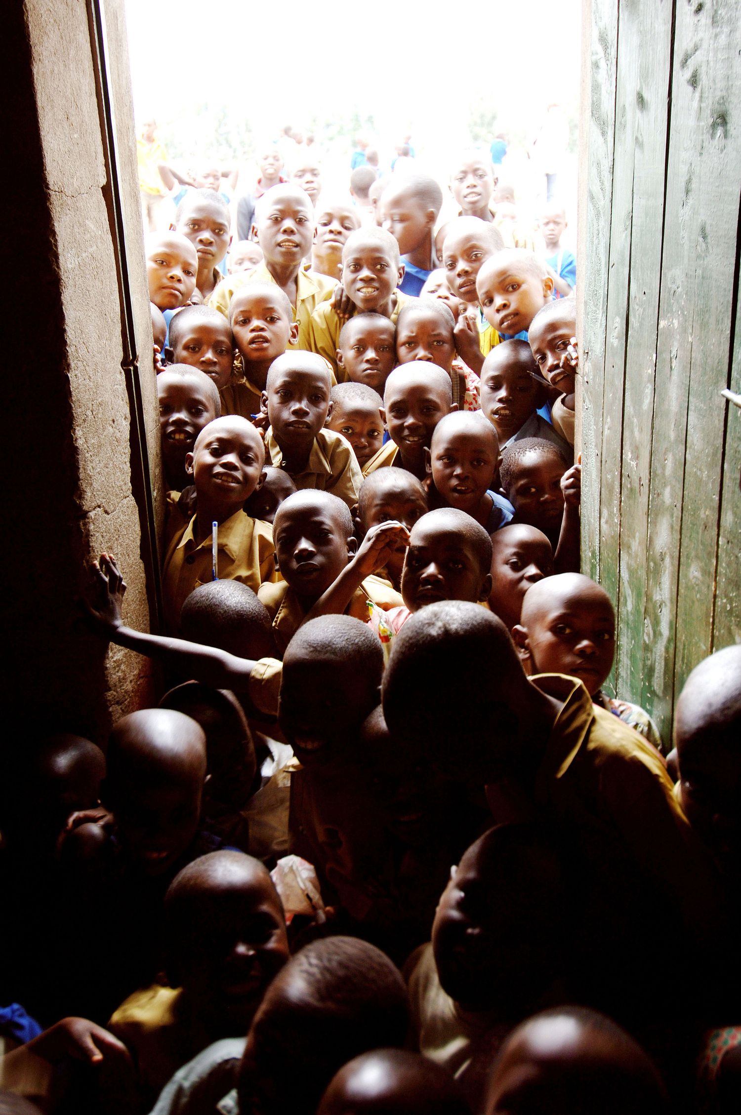 A crowded doorway filled with children looking curiously through the entrance of a classroom. Working with Oxfam in Rwanda by John Ferguson