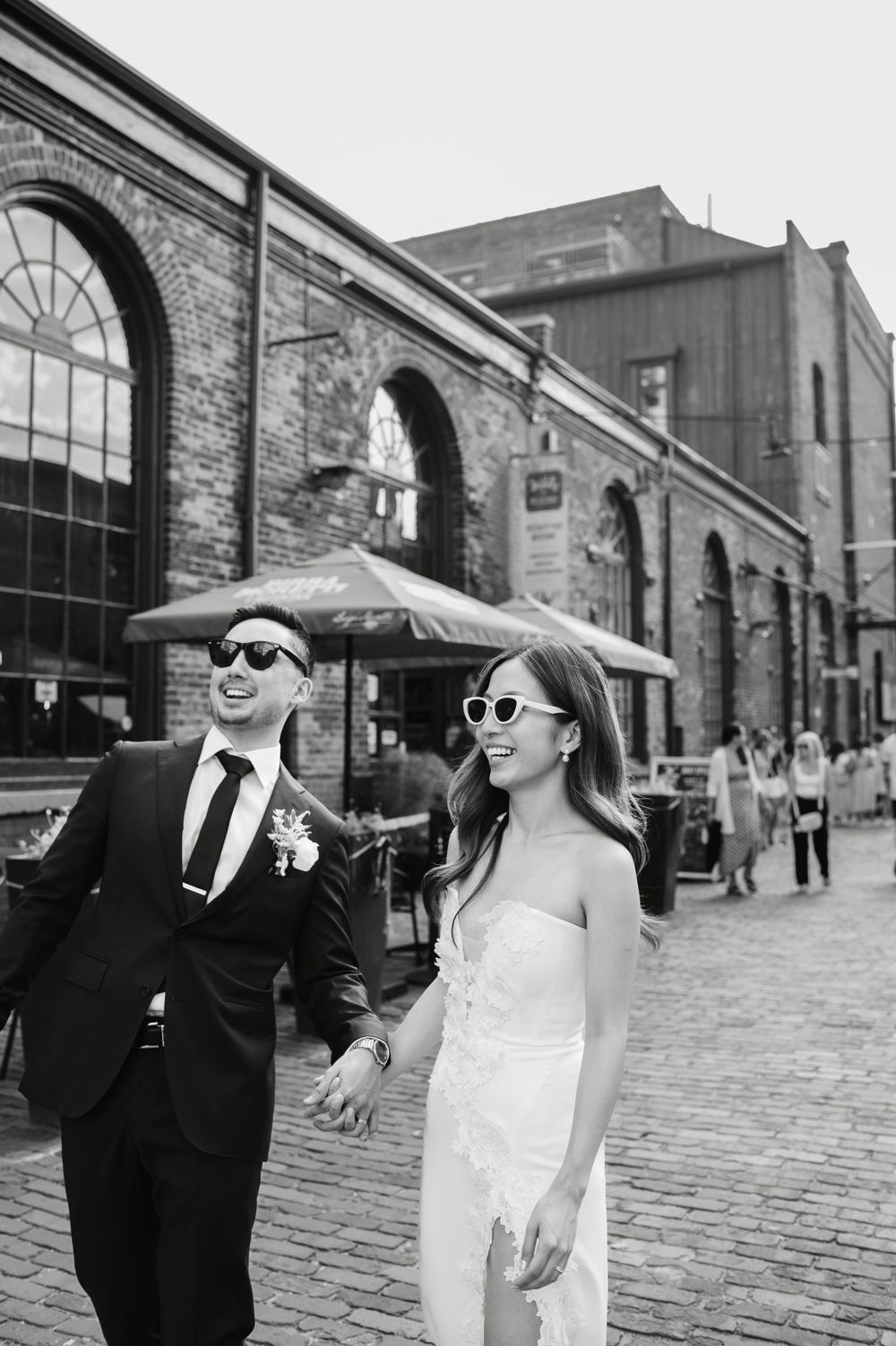 Wedding couple walking and laughing together in Toronto’s Distillery District, both wearing sunglasses, documentary-style wedding photos