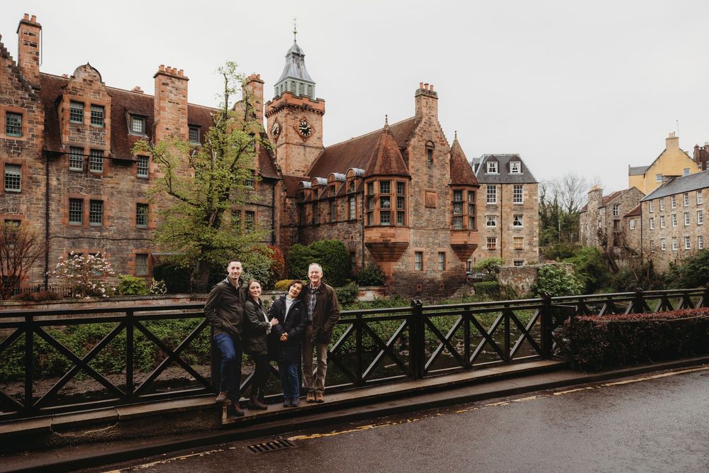 A couple stands on a bridge in Edinburgh with historic university buildings and stone architecture in the background.