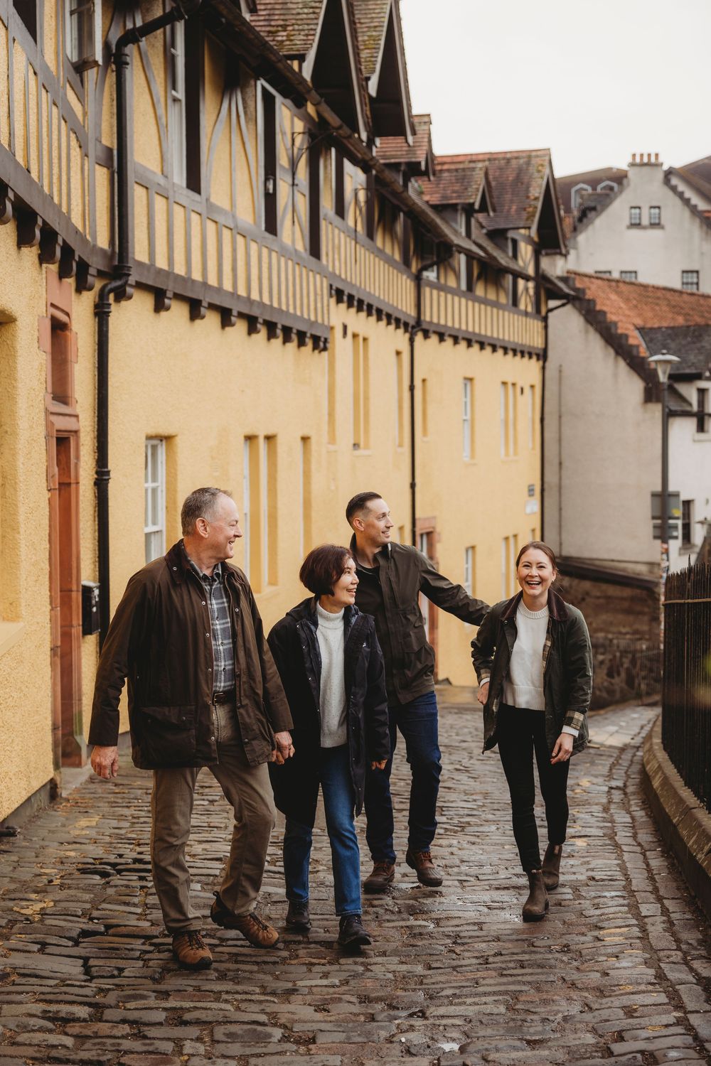 A group walks together down a charming cobblestone street lined with historic yellow Tudor-style buildings in England.