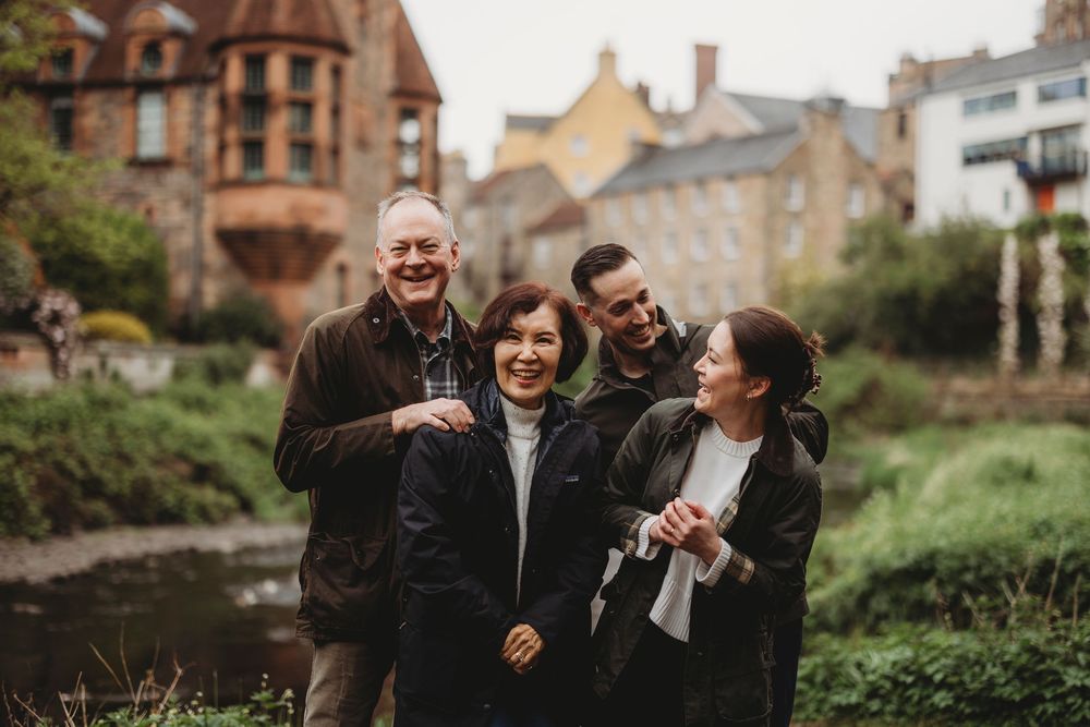 A group of diverse friends share joyful laughter together on a misty autumn day in Edinburgh with historic buildings behind them.