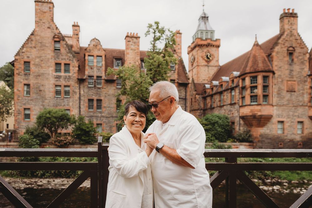 A couple sharing a romantic moment on a bridge in front of Dean Village's historic architecture in Edinburgh, Scotland.