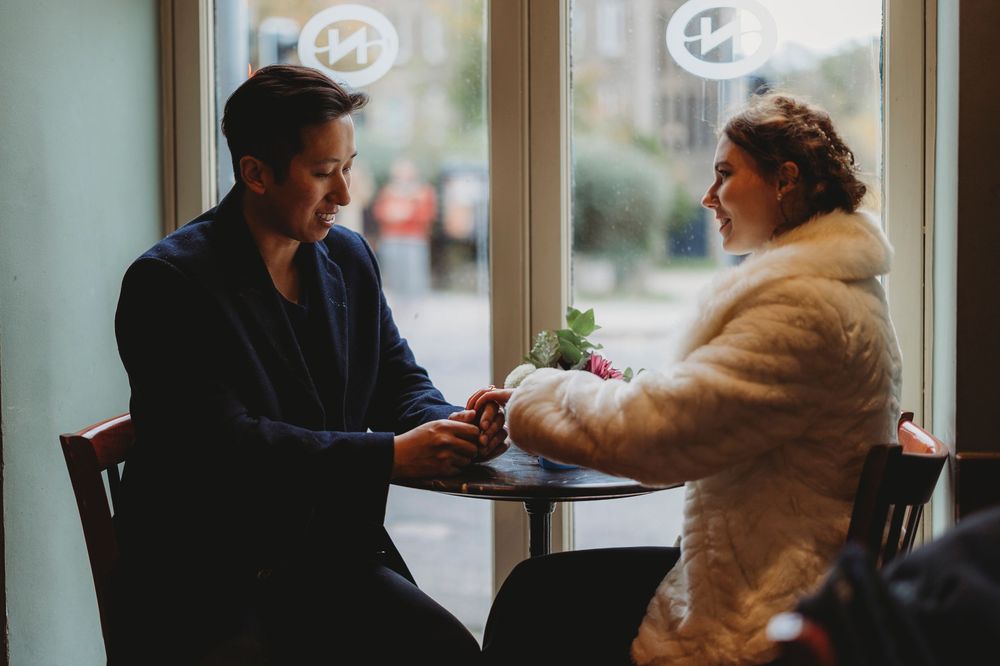 Two people sitting at a cafe table near a window having an intimate conversation in warm lighting.