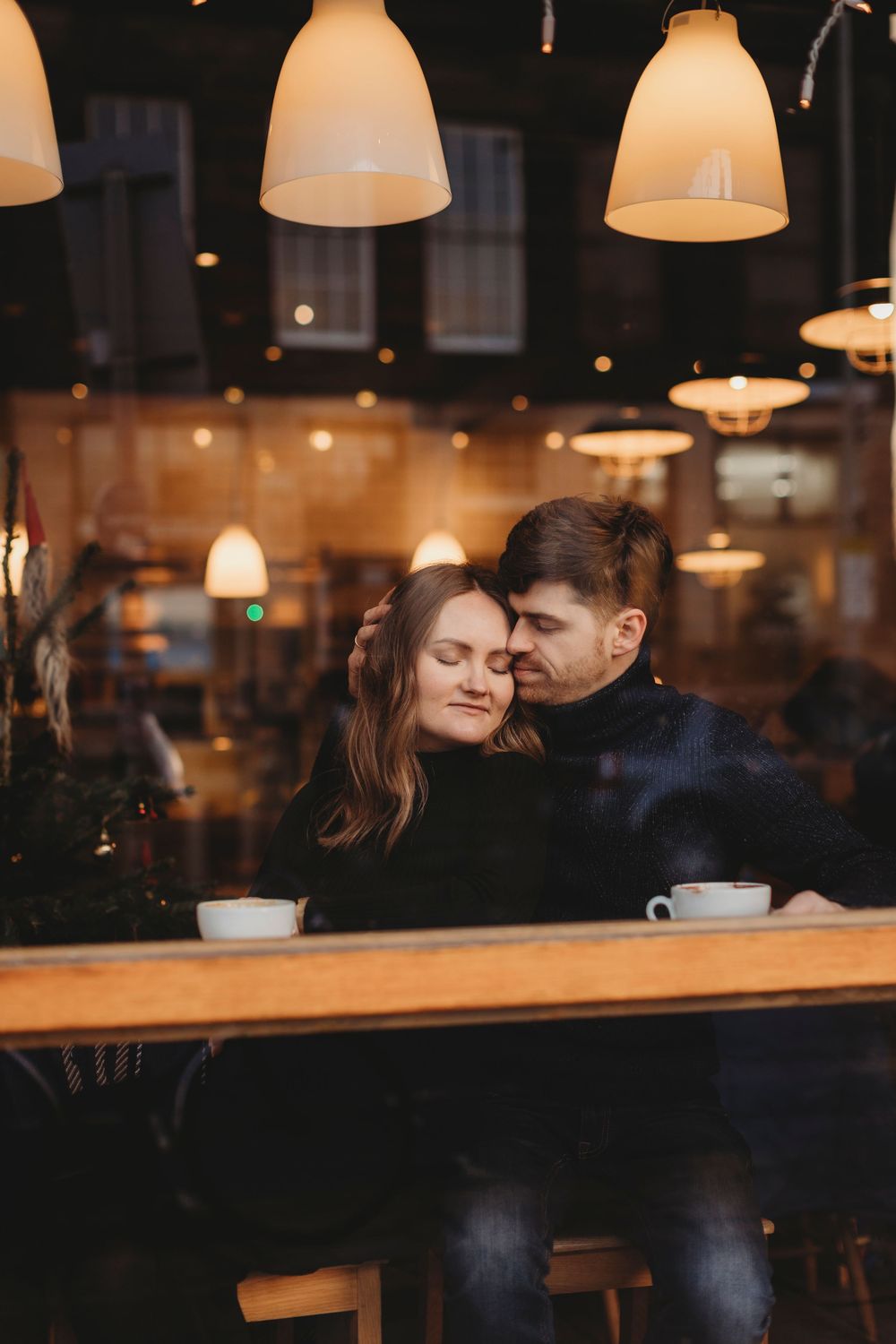 Romantic couple sharing intimate moment at cozy cafe with warm lighting and pendant lamps overhead.