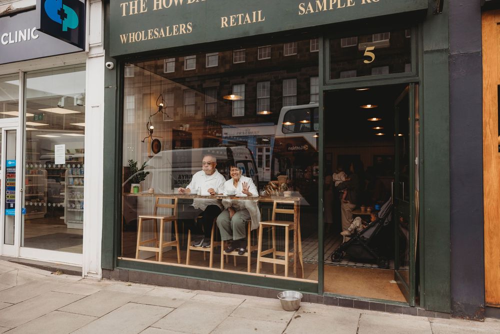 Small coffee shop storefront with window seating and customers enjoying drinks at wooden bar stools in Toronto.