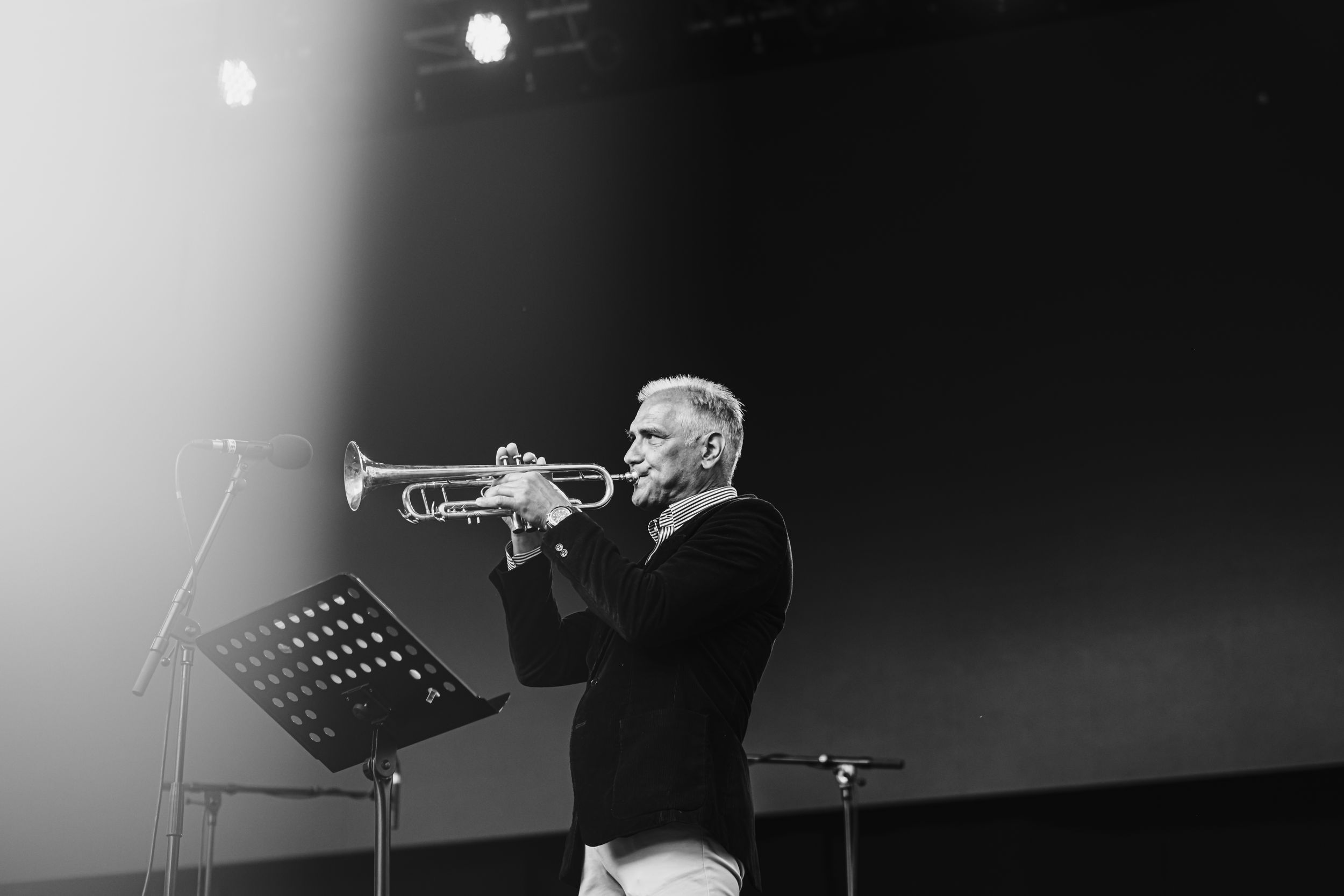 Black and white photo of trumpet player performing on dimly lit concert stage.