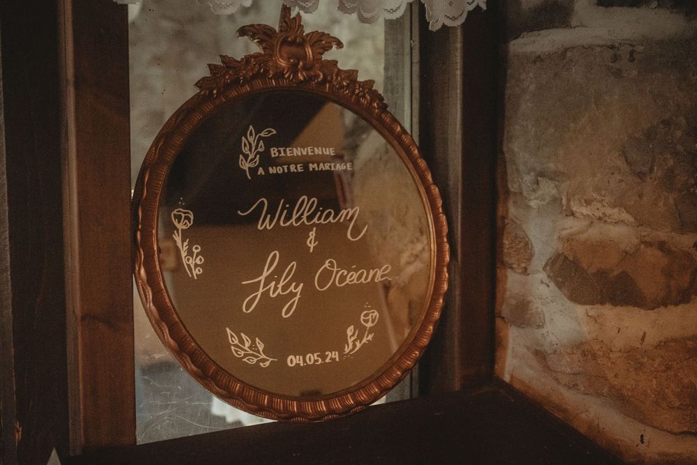 Ornate vintage mirror with wedding details written in elegant calligraphy against stone wall.