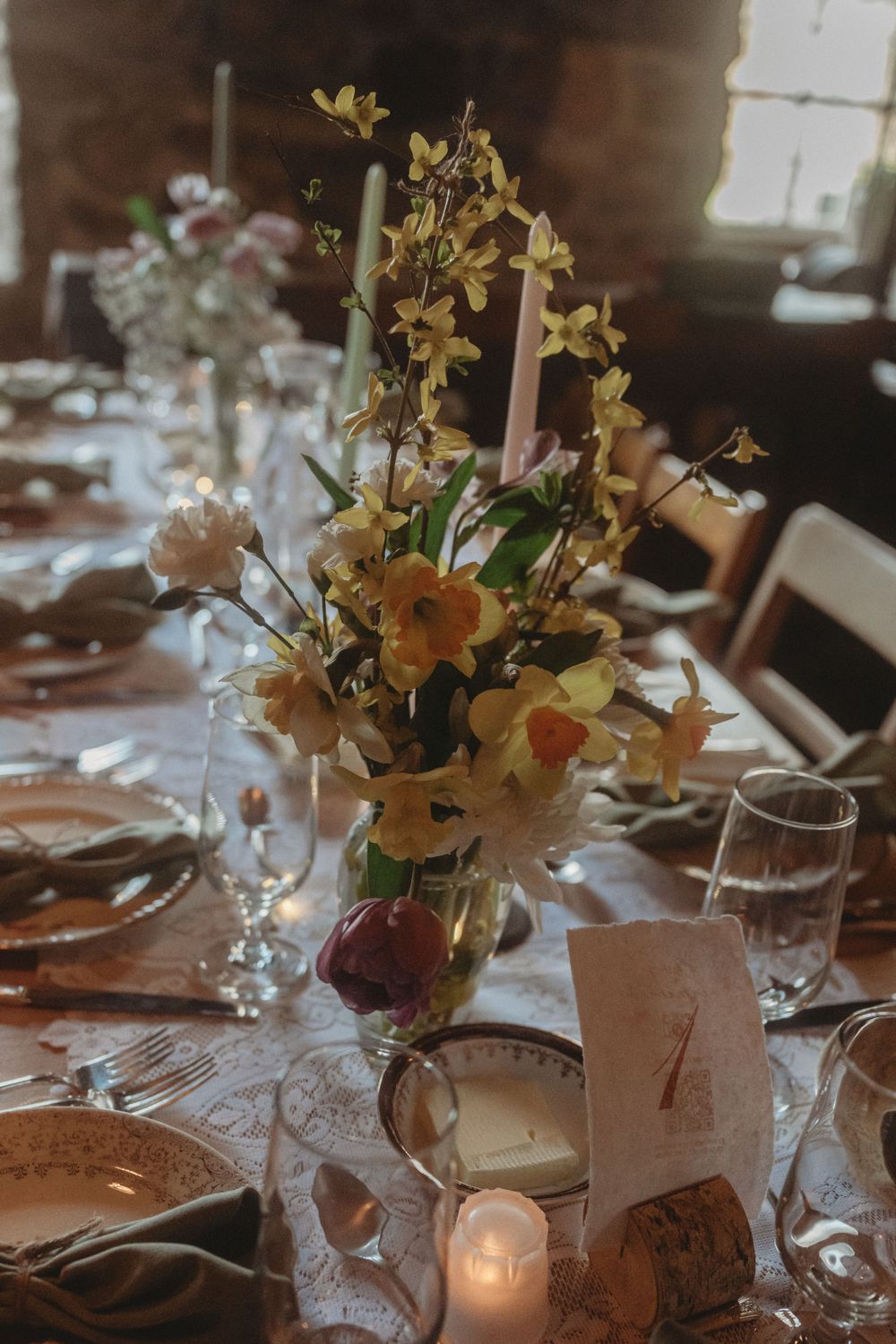 Elegant wedding table setting with tall yellow floral centerpiece and glowing candles.