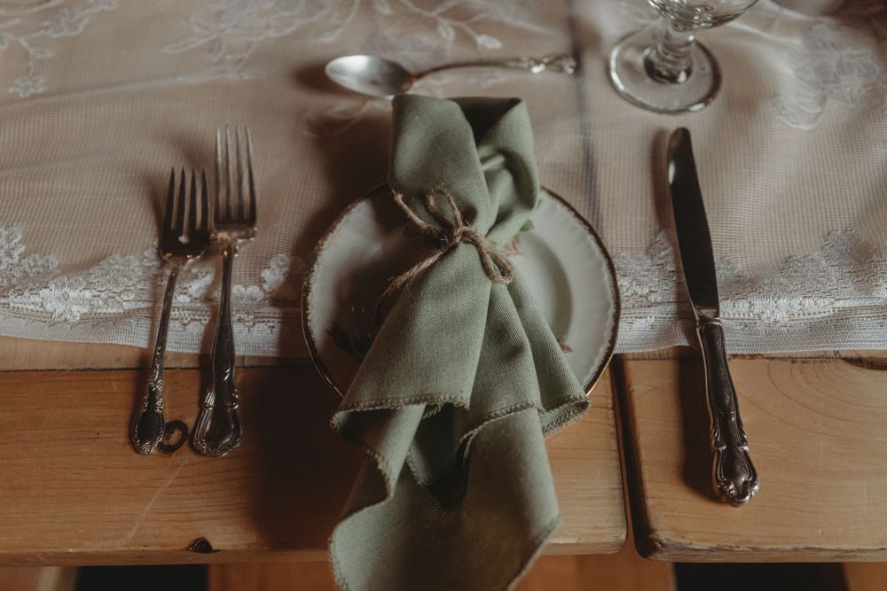 Place setting with sage green napkin and vintage silverware on wooden table.