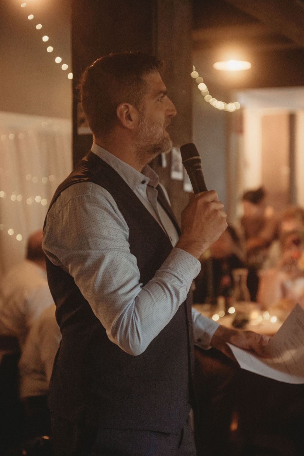 Wedding speech being delivered in dimly lit reception venue with string lights.