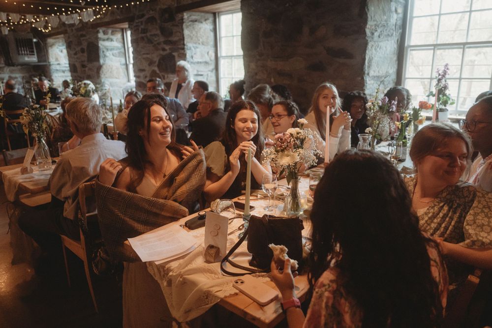 Wedding reception guests enjoying dinner and conversation in rustic stone venue.