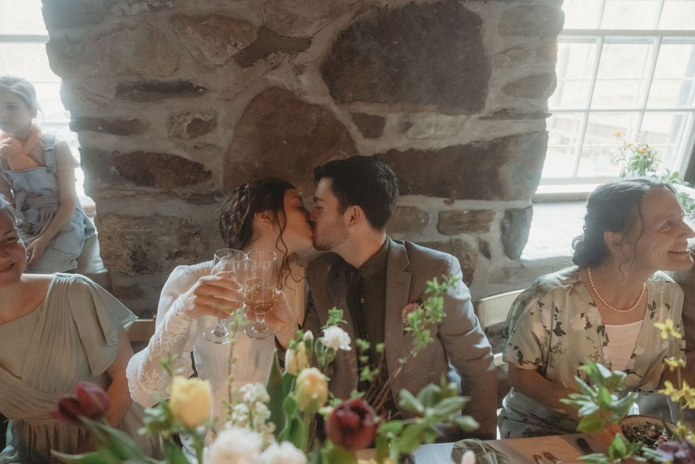 Intimate moment at wedding reception with couple seated at rustic stone wall table with floral centerpieces.