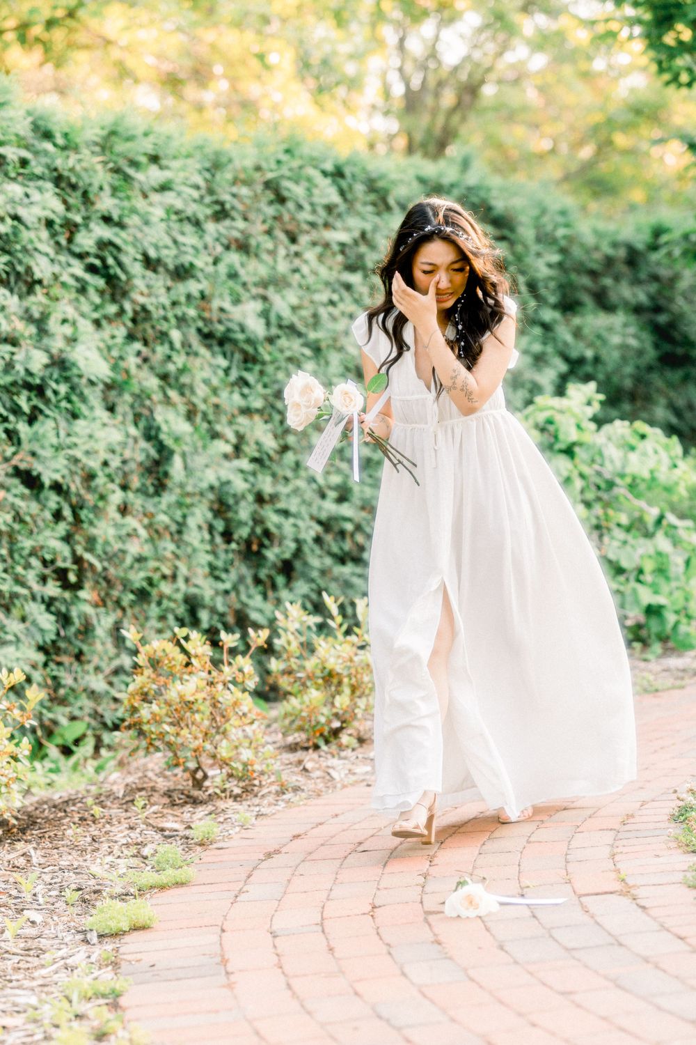 A woman in an ethereal white dress strolls through a lush garden pathway.