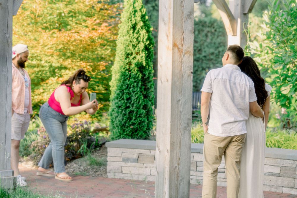 A couple enjoys a romantic moment in a garden setting with stone pillars and greenery.